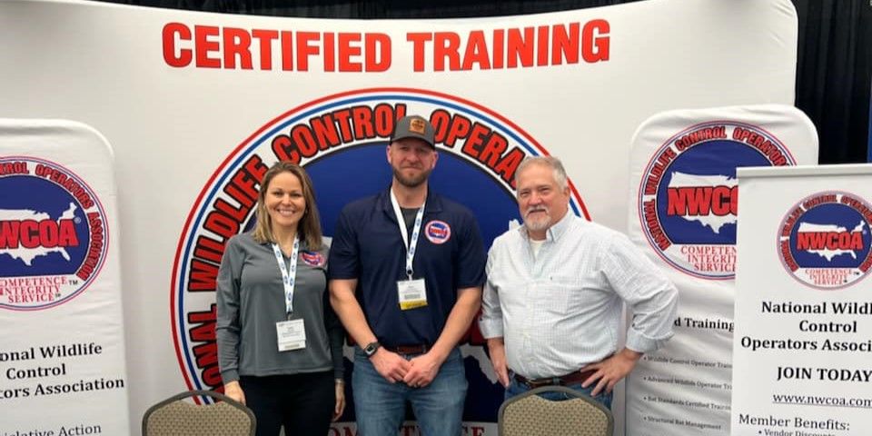 Three people standing in front of a NWCOA Certified Training banner at a NWCOA event.