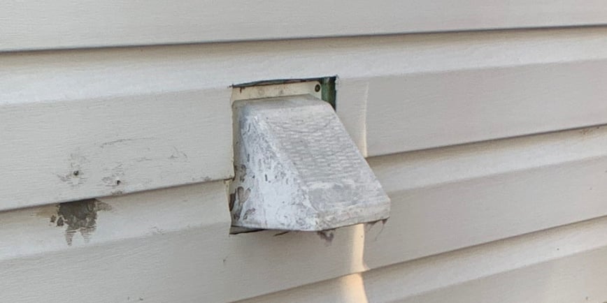 A hooded dryer vent sticking out of the side of a house with gray siding.