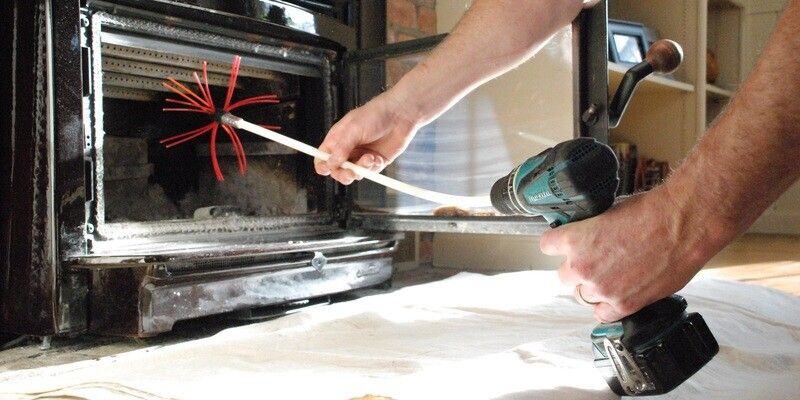 A man using a Gardus SootEater to clean the inside of a wood fireplace insert.