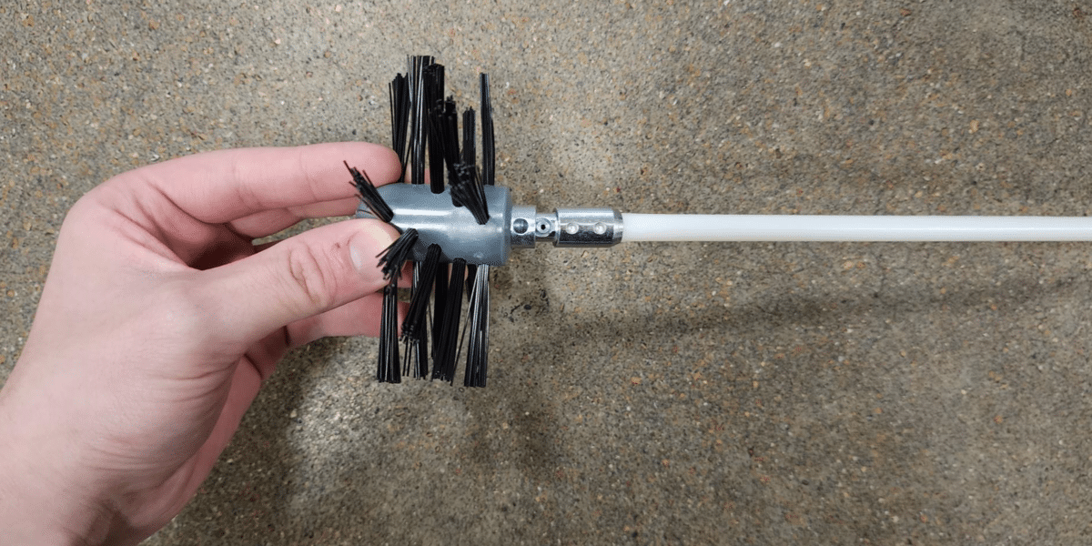 The auger brush head of a dryer vent cleaning kit being connected to one of the kit's rods via a button-style connector