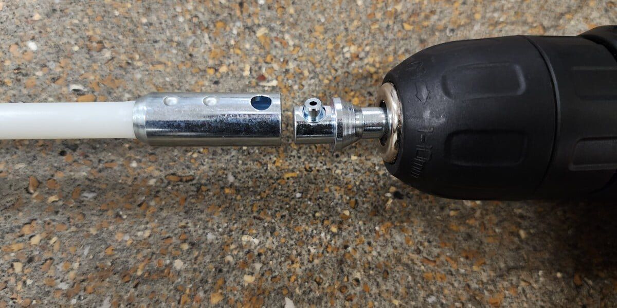 A dryer vent cleaning kit rod with a button-style connector about to connect with the drill bit connector attached to a drill