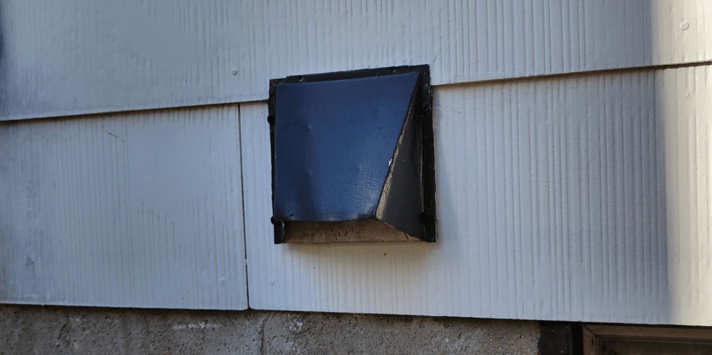 A black dryer vent cover on a house with white siding