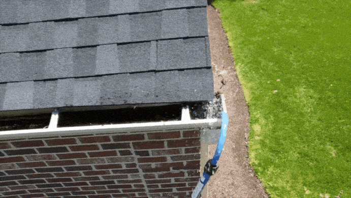 A GutterSweep rotary cleaning tool being used to clean dirty, muddy water from a downspout.