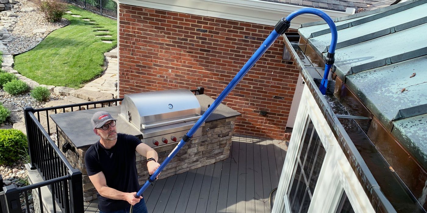 A man using a the water jet nozzle on a GutterSweep to clean gutters from his patio.