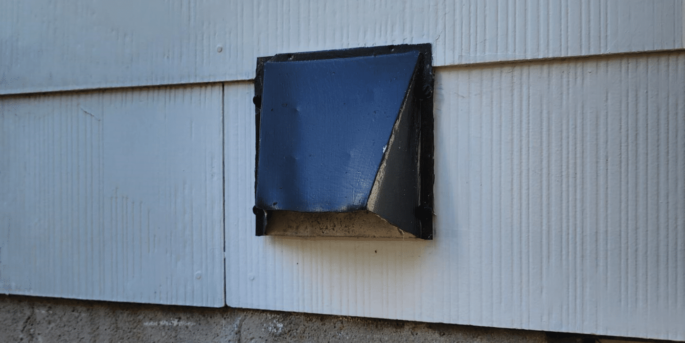 A black, aluminum, hood-style dryer vent cover installed on a home with white siding