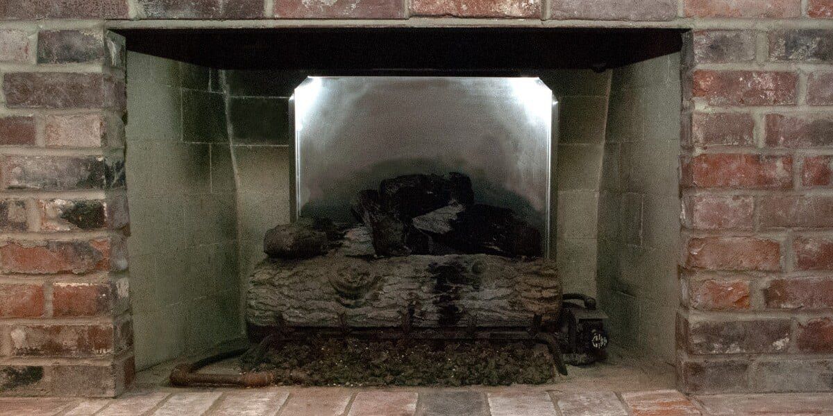A stainless steel Liberty Foundry Co. fireback installed in a fireplace behind a grate full of logs