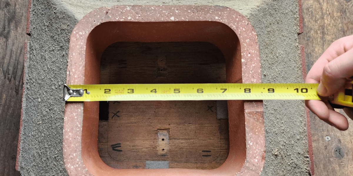 A measuring tape across a square flue tile measuring 8.5 inches