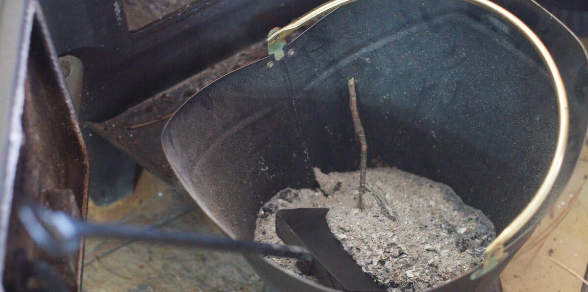 A bucket full of ashes from an extinguished fire with a small black shovel in it