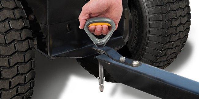 A hand reaching down to pull a Good Vibrations Quick Connect Hitch Pin out of a lawn tractor hitch.