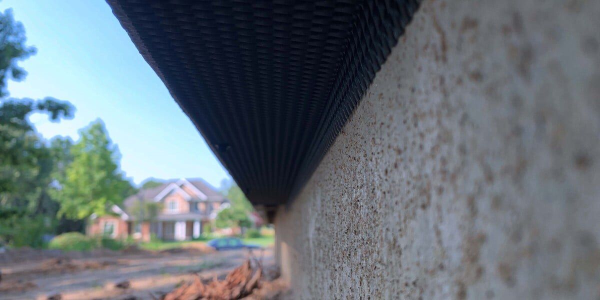 L-Mesh Pest Armor installed near the foundation of a home under a rainscreen siding gap with a large suburban house in the background