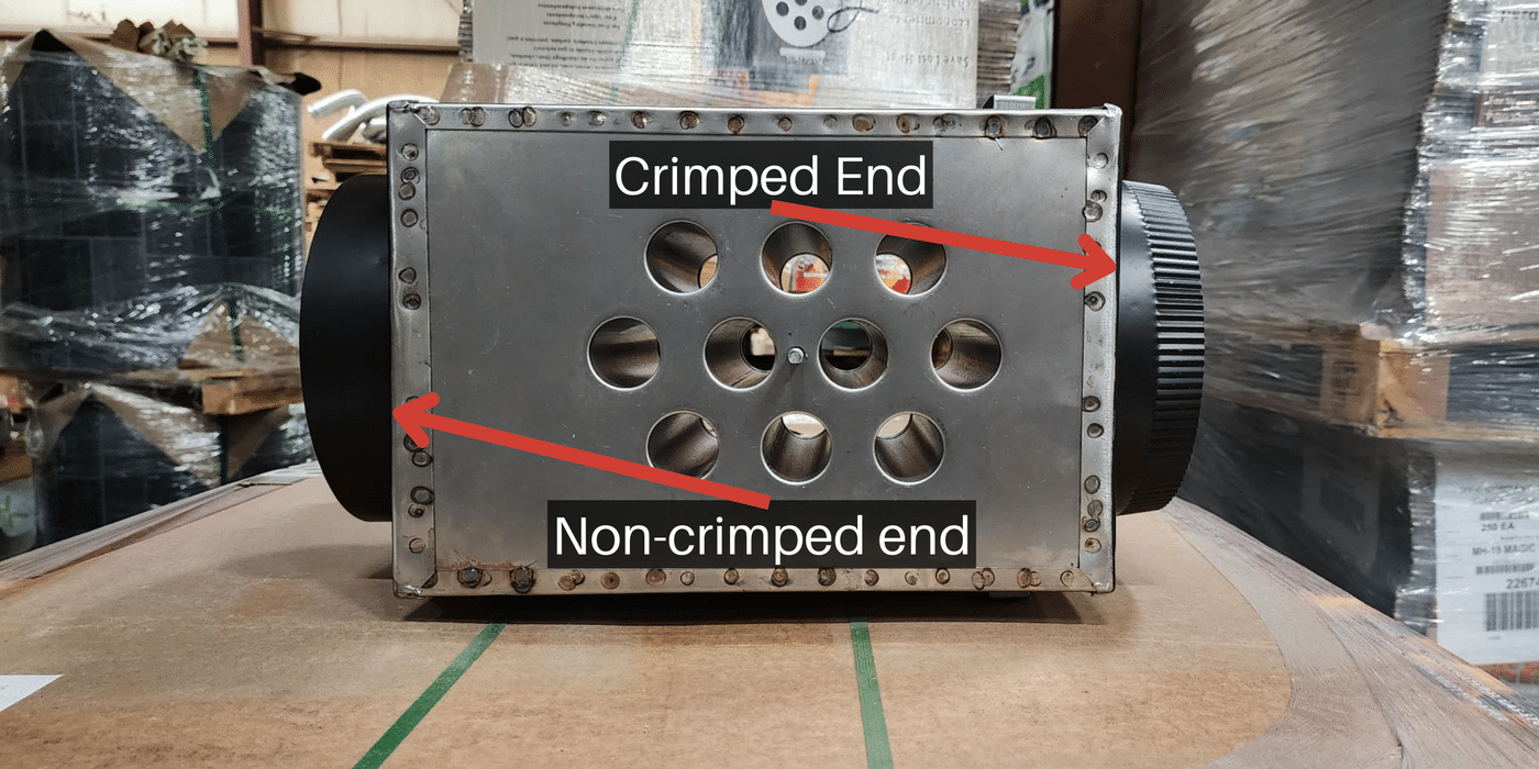 A stripped-down Magic Heat heat reclaimer on its side with white text and red arrows indicating the crimped end and non-crimped end of the flue pipe connections