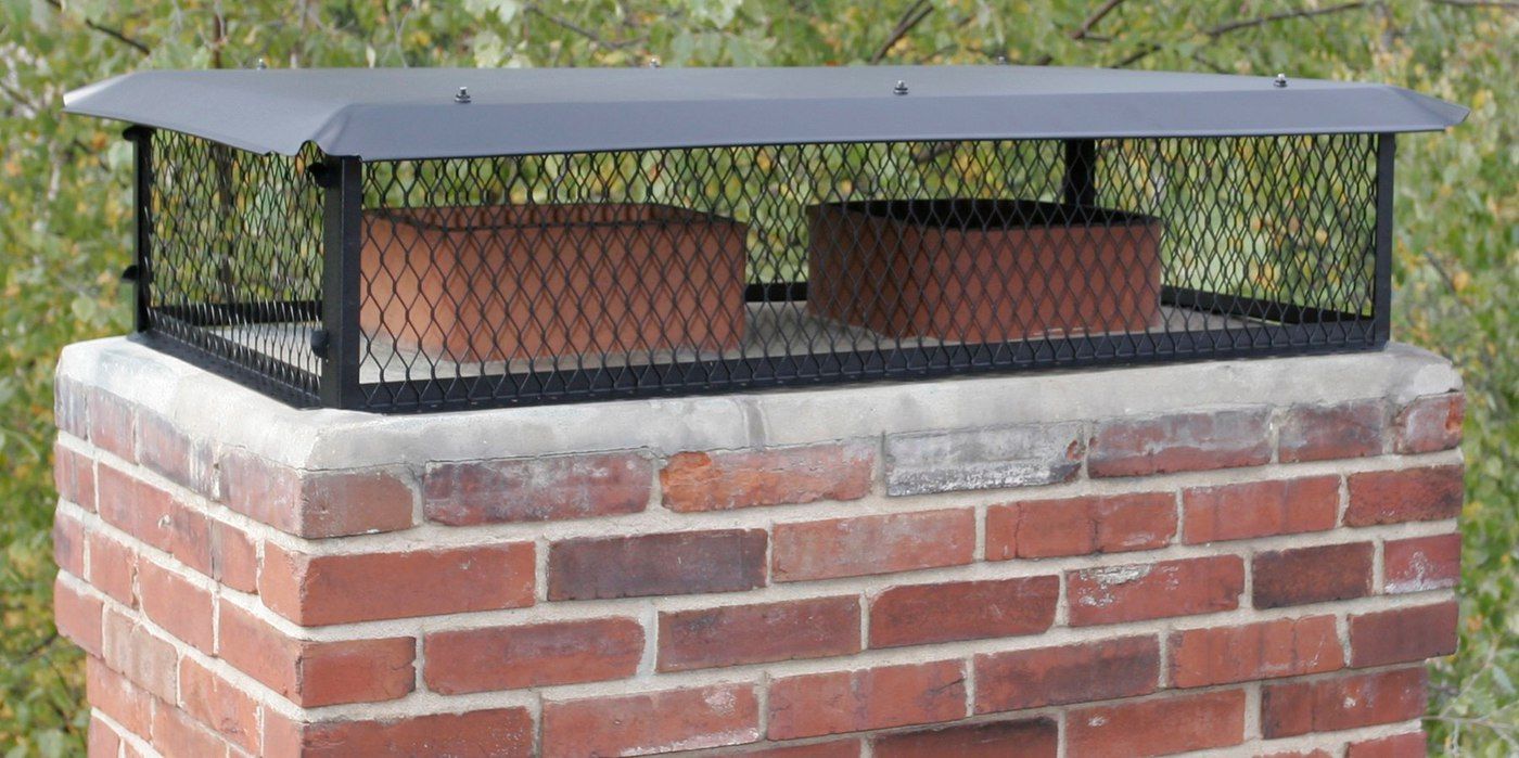 A black galvanized multi-flue chimney cap installed on a chimney crown with two flues against a background of foliage