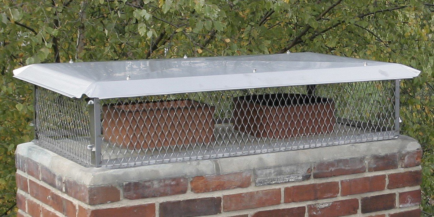 A multi-flue stainless steel chimney cap installed on a chimney crown with tree limbs in the background