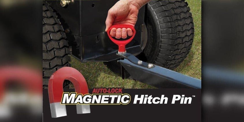 A man holding onto a Good Vibrations Auto-Lock Magnetic Hitch Pin that's being used to connect a dump cart to a lawn tractor.