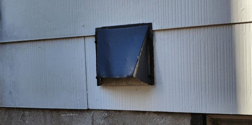 A black, hood-style dryer vent on the side of a house with white wooden siding.