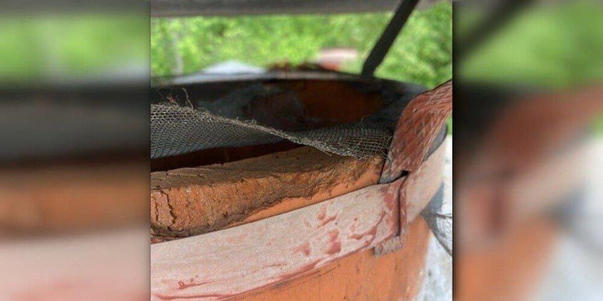 A close-up of an old, rusted, round chimney flue. The animal exclusion hardware cloth on the cap is broken and chewed through.