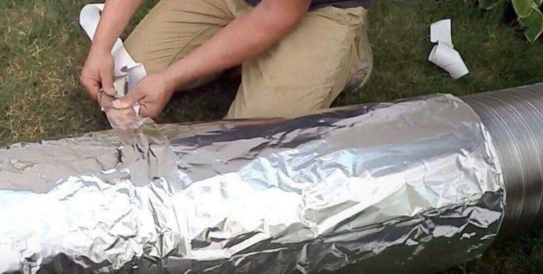A man on a lawn wrapping a chimney flue liner with insulation.
