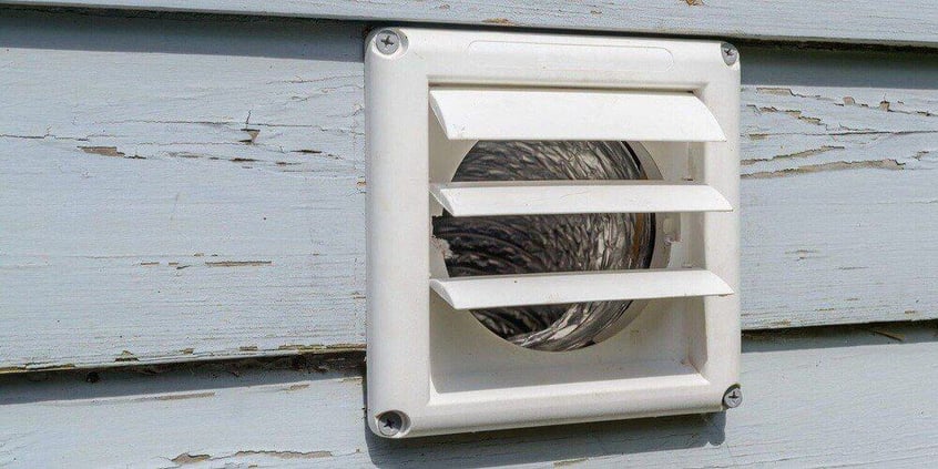 A white dryer vent cover with louvres installed on the side of a home with grayish-blue wood siding.