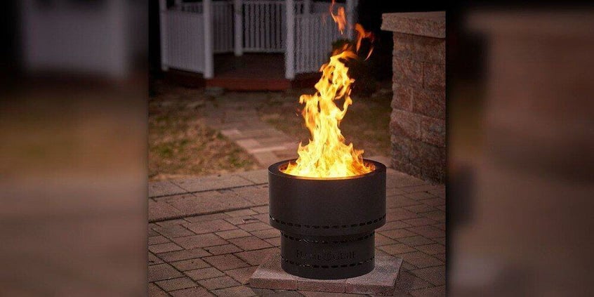 A Flame Genine smokeless fire pit with a fire roaring inside it. The fire pit rests on a back patio with a gazebo visible in the background.