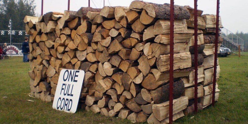 A cord of firewood sitting on a makeshift firewood rack. A sign reading "one full cord" with all capital letters rests against the firewood.