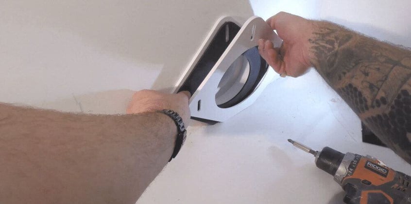 A POV shot from the perspective of a man installing a SnugDryer dryer vent connection kit into the drywall of a home. 