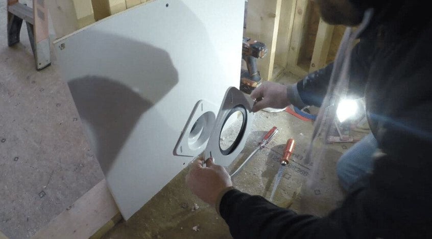 A man installing a SnugDryer dryer vent connection kit into the drywall of a home that's under construction.