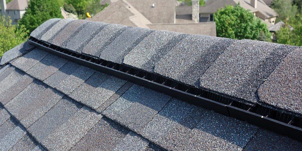 Ridge vents on a roof with gray shingles and a suburban neighborhood in the background