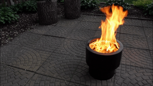 A looping GIF showing a smokeless fire pit in use on a garden patio with mulch landscaping in the background