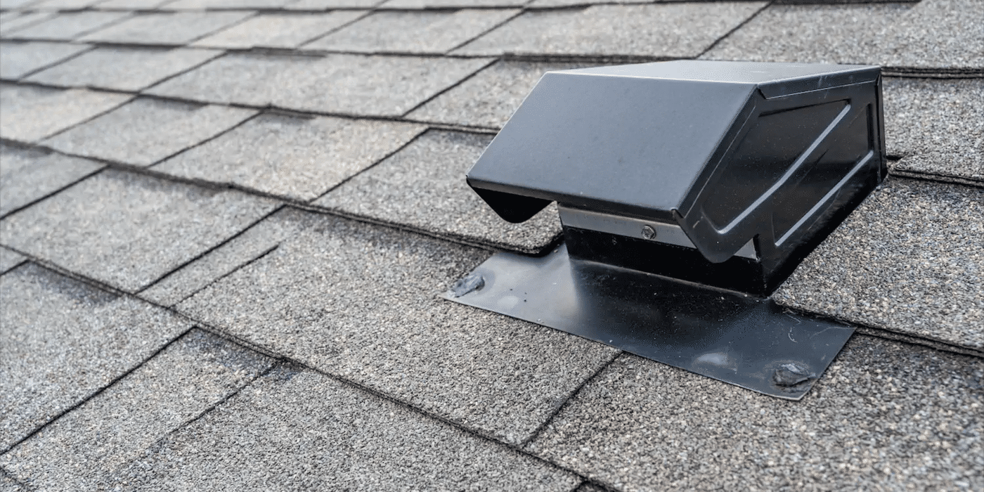 A close-up of a black, static roof vent protruding from a roof with gray shingles