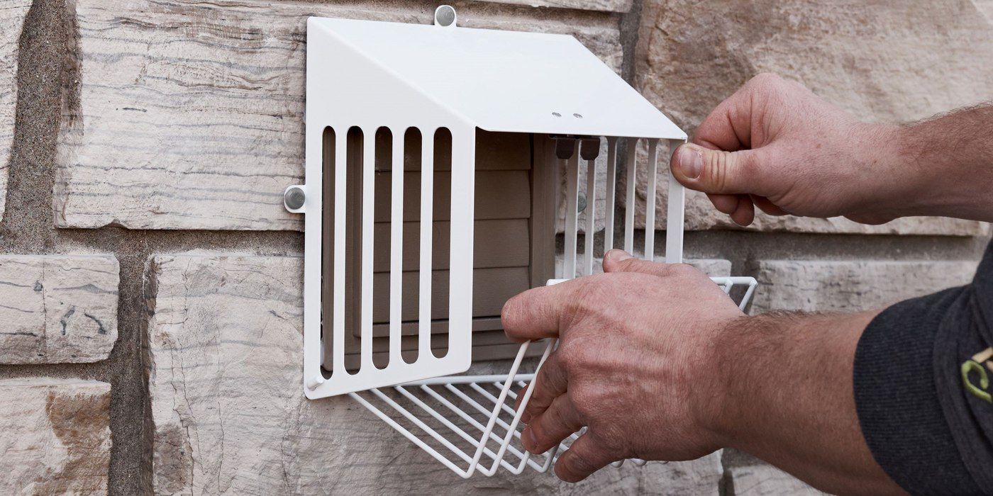 A man opening a HY-GUARD EXCLUSION Steel Dryer Vent Exhaust VentGuard installed on a house with stone siding