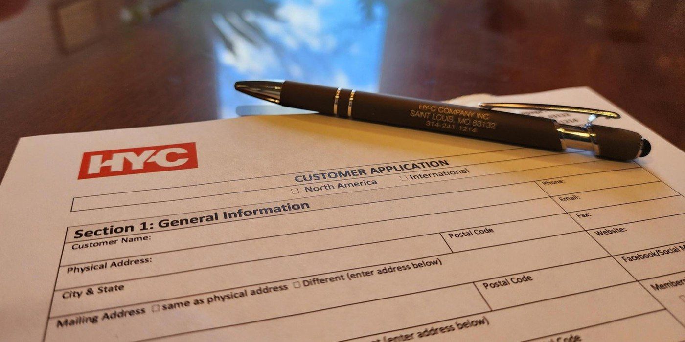 A HY-C customer application resting on a wooden desk with a pen sitting on the application