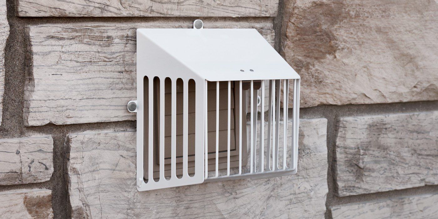A white universal code-compliant dryer vent guard installed on a house with stone siding