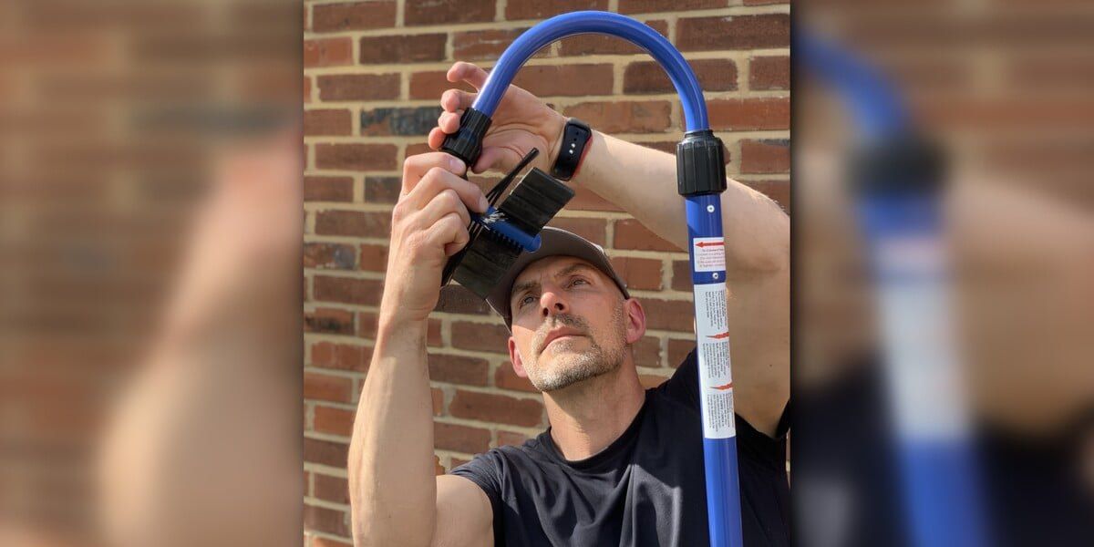 A man attaching the rubber paddle brush head to the curved tubing of a GutterSweep with a brick wall in the background