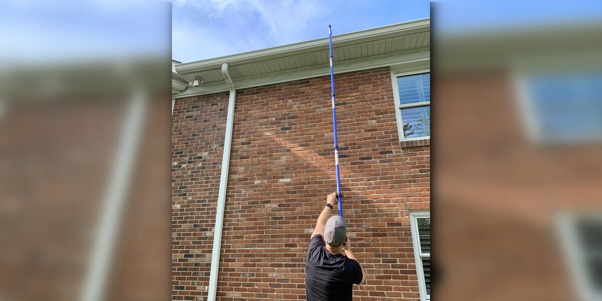 A man using a GutterSweep supplemented by a GutterSweep extension kit to clean gutters on a two-story brick building
