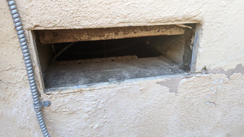 An uncovered foundation vent on the side of a home showing an exposed crawl space
