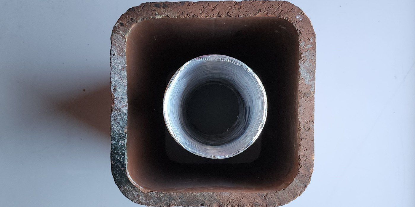 A top-down view of a round chimney liner inside a square chimney flue tile