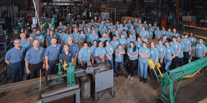 The HY-C company leadership team and factory staff pose for a picture together on the plant floor. Everybody is wearing matching blue HY-C shirts.