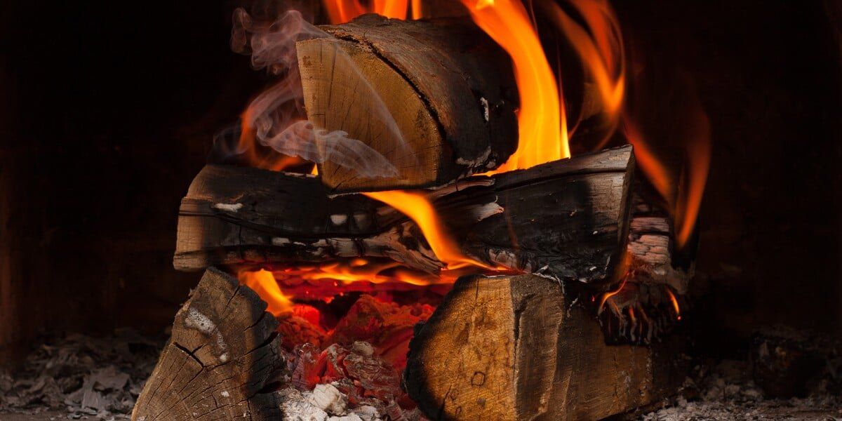 A burning pile of about six logs with ash around them against a black background