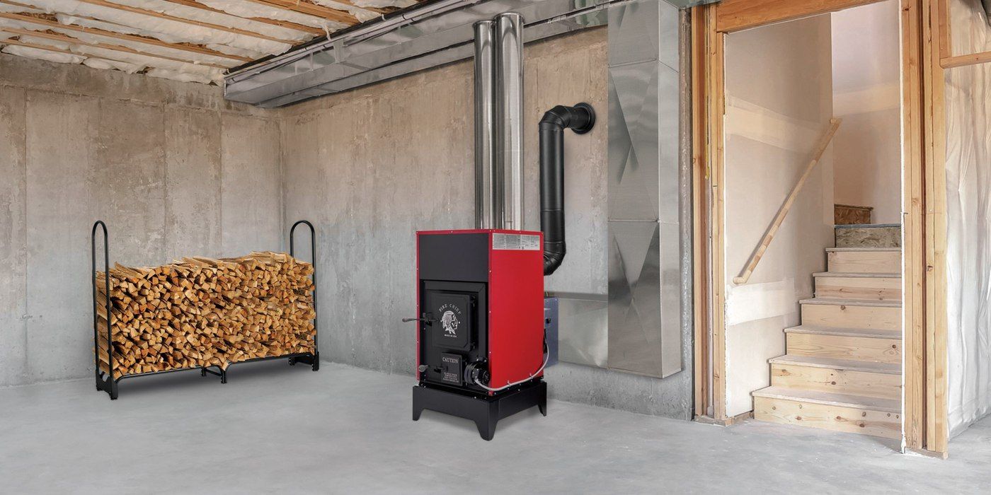 A Fire Chief FC1000E wood burning furnace installed into ductwork in an unfinished basement with a full, half-cord log rack to the right
