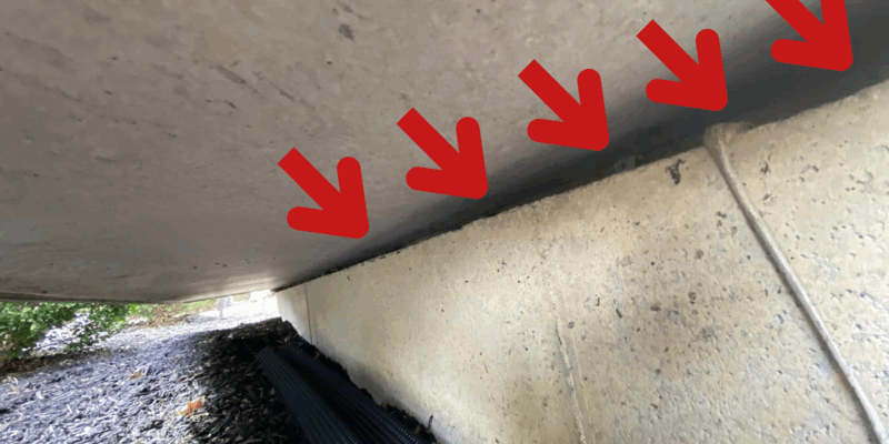 A shot of the underside of a home with the view of a gap in the foundation. Five red arrows have been added to point out the gap.
