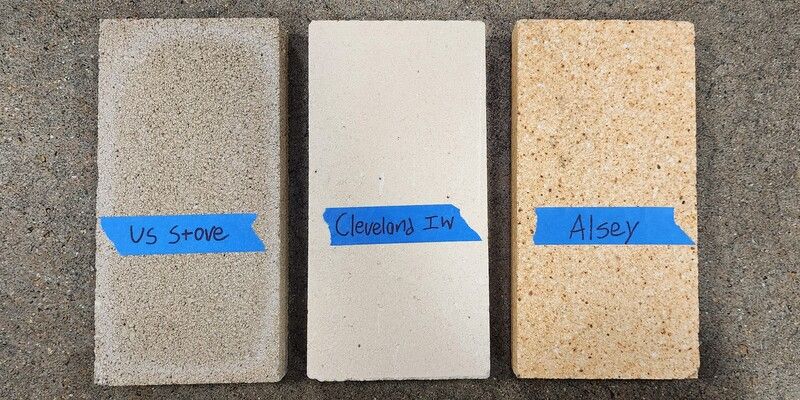 A US Stove, Cleveland Iron Works, and Alsey Refractories Co. firebrick laying side-by-side on a floor. They are labeled with blue painter's tape.