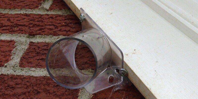 A plastic, one-way bat cone installed on the side of a brick home right under the roof.