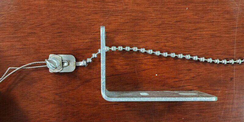 A chimney damper steel cable attached to the damper's ball chain handle which itself is attached to the firebox bracket, all lying on a wooden table.