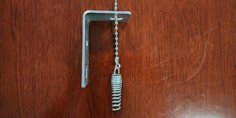 A chimney damper firebox bracket and ball chain handle lying on the surface of a wooden table.