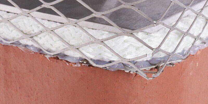 A close-up of the gasket of a Draft King chimney damper installed with silicone beading over the cage of a Draft King Universal Chimney Cap.