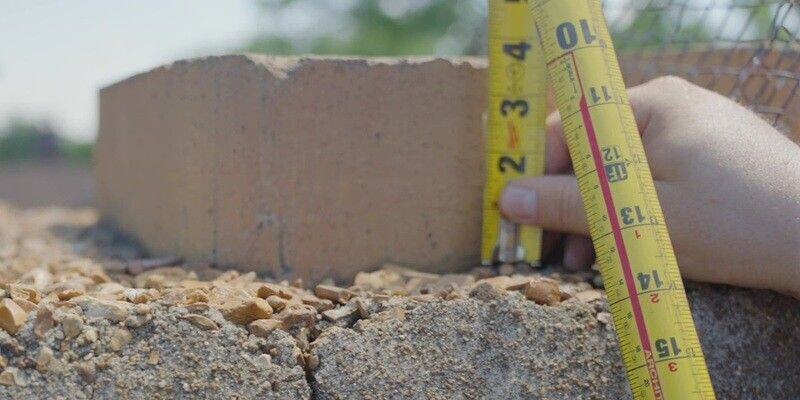 A man using a tape measure to measure the height of a chimney flue tile.