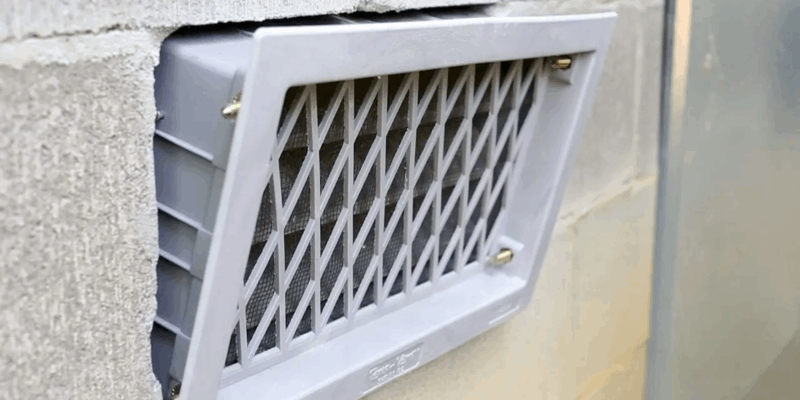 A foundation vent installed in a cinder block foundation. The vent is unsecure and beginning to come loose from the foundation.