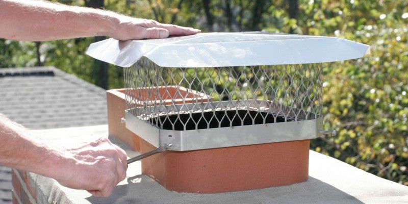 A man installing a stainless steel Draft King chimney cap on a chimney.
