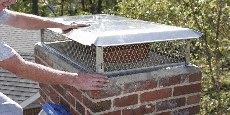 A man installing a Draft King Stainless Steel Multi-Flue Chimney Cap on a chimney with two flue tiles.