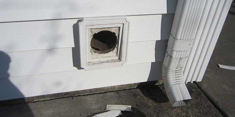 A dryer vent on the side of a home. The vent is missing its protective louvers. The vent rests about 12 inches above the ground.